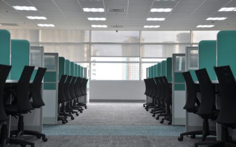 Modern corporate office interior with rows of workstations, ergonomic chairs, and large windows, showcasing a clean and organized workspace environment suitable for business operations.